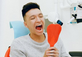 Man in dental chair looking in mouth using a mirror