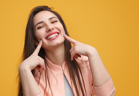 a woman in Lewisville pointing at her new dental crowns