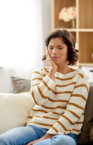 Woman experiencing toothache sitting on couch at home