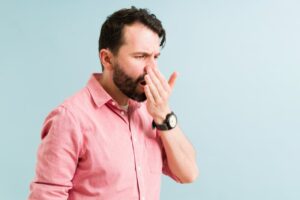 Young man checking his breath with hand to mouth.