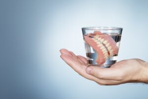 Hand holding set of dentures in a glass of water.